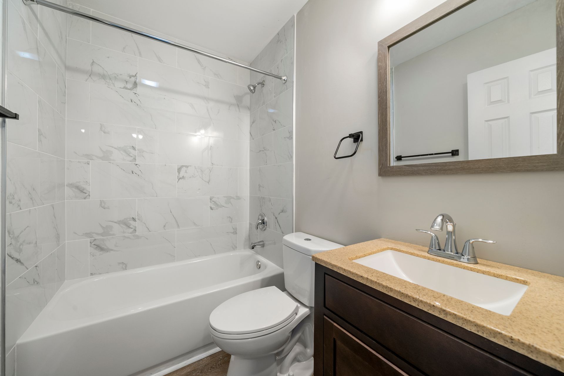 Small bathroom with white tub and shower, toilet, and vanity with mirror and sink.