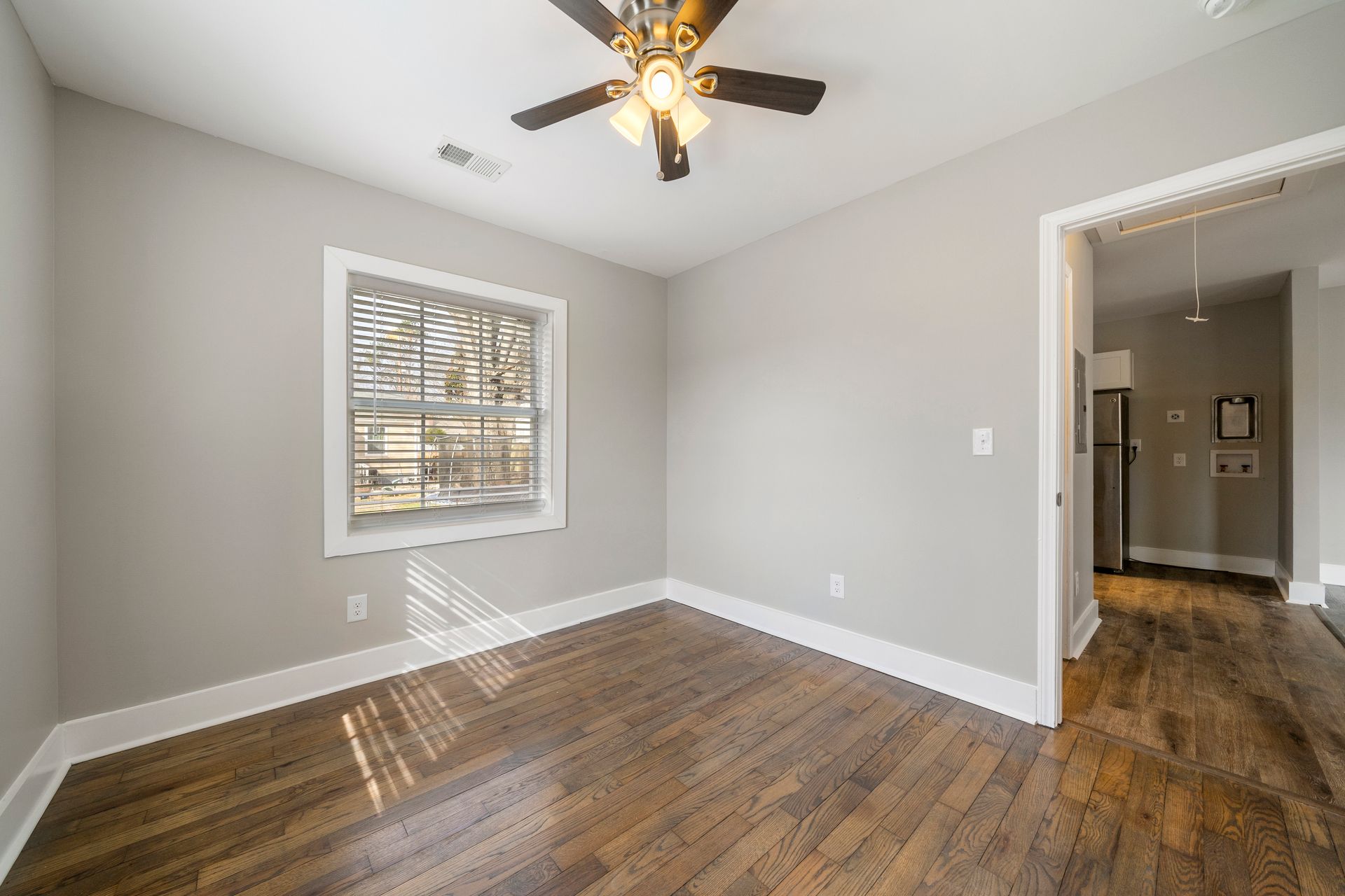 Empty bedroom with gray walls, wood floors, ceiling fan, and window with white blinds