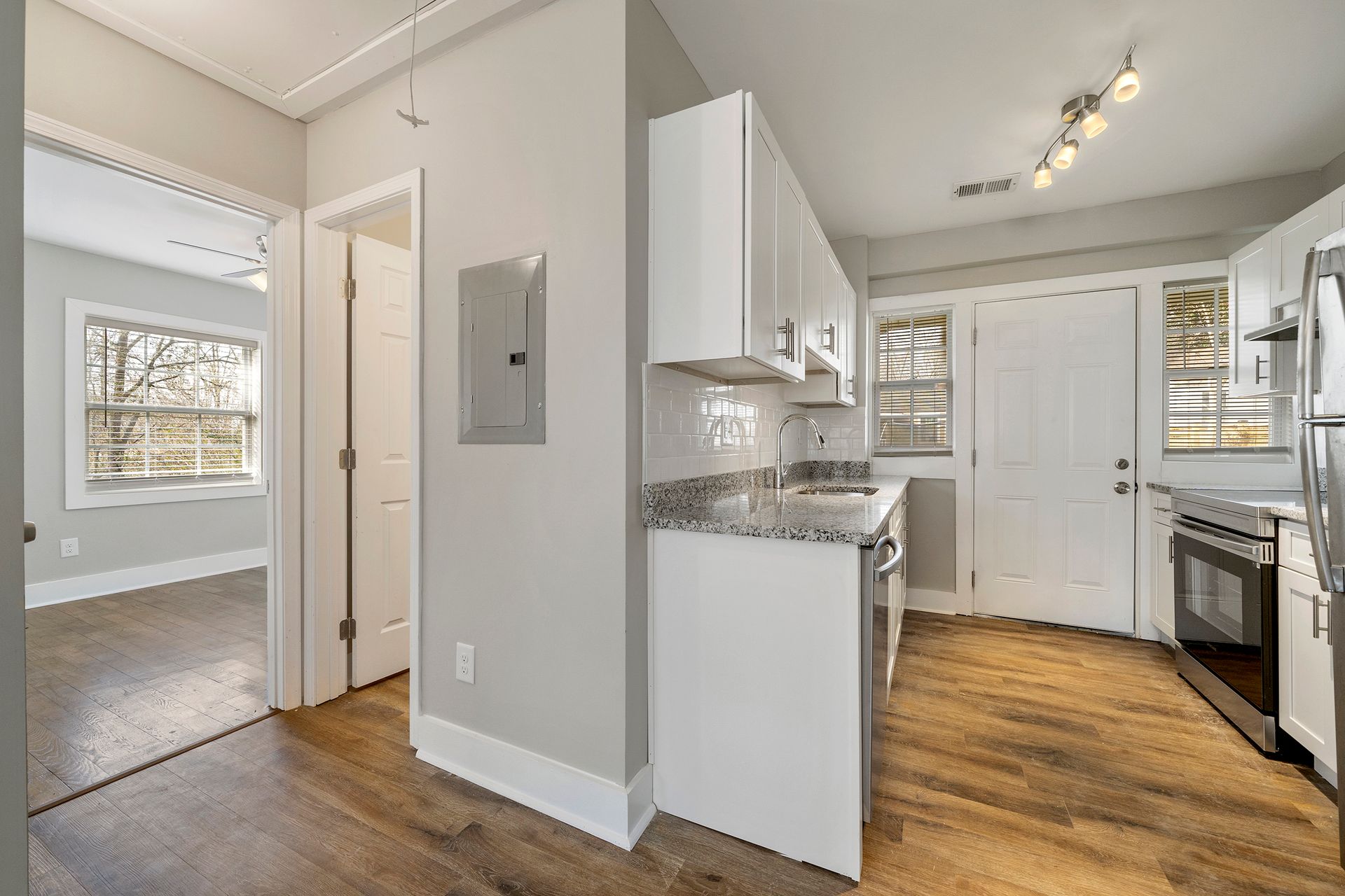 Bright kitchen with white cabinets, granite counters, and hardwood floors, open to a carpeted living area