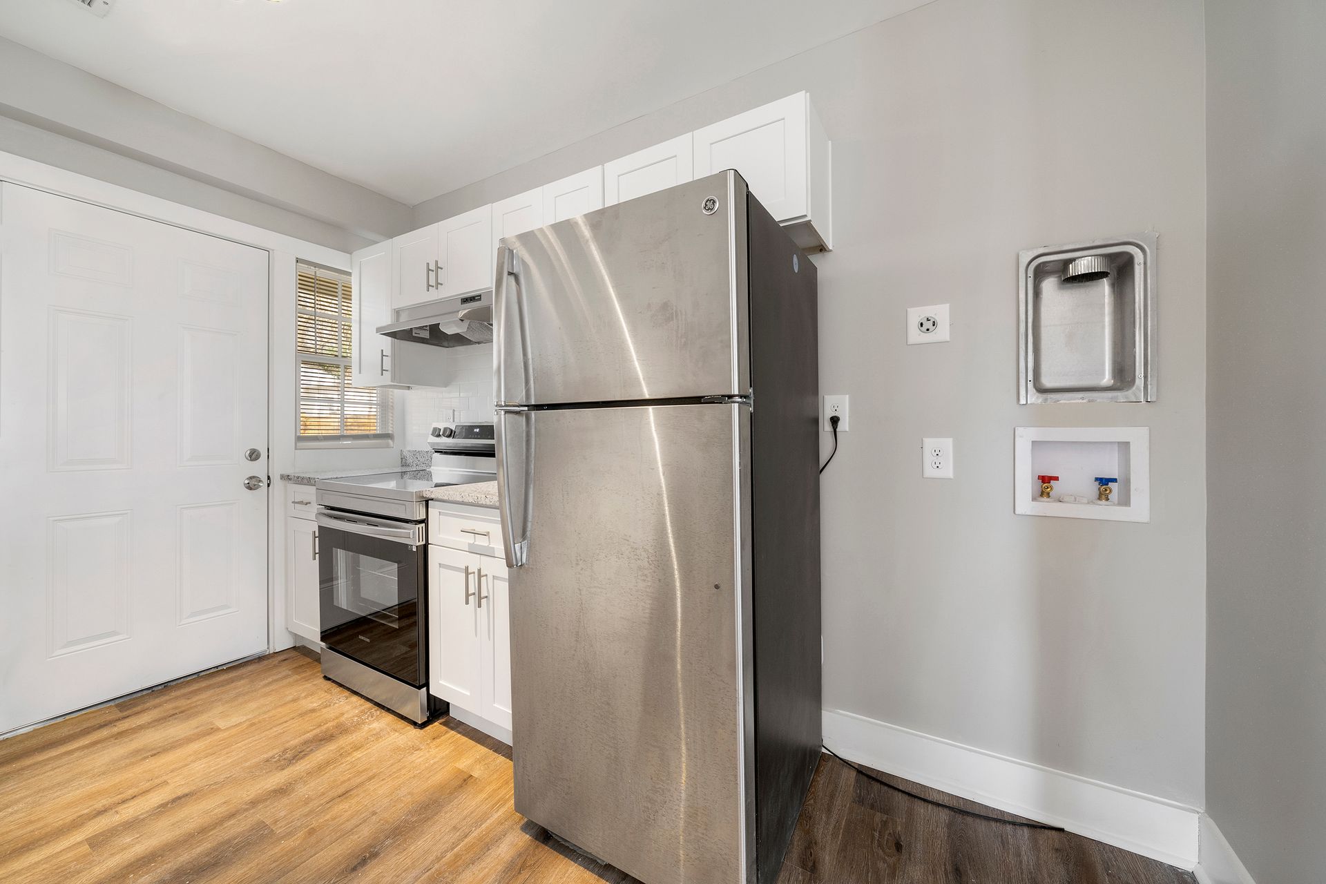 Compact kitchen with stainless steel refrigerator, stove, and white cabinets on hardwood floors
