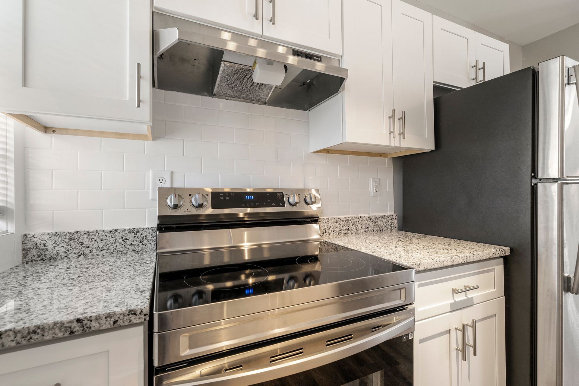 Modern kitchen with stainless steel stove, range hood, refrigerator, and white cabinets