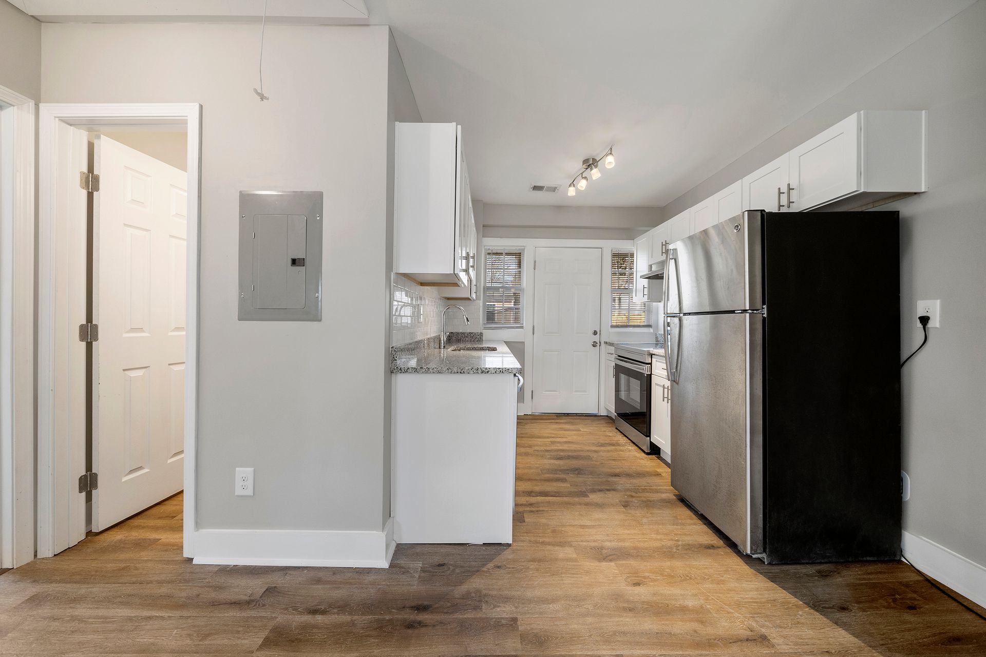 Empty apartment kitchen with white cabinets, stainless refrigerator, and wood floors