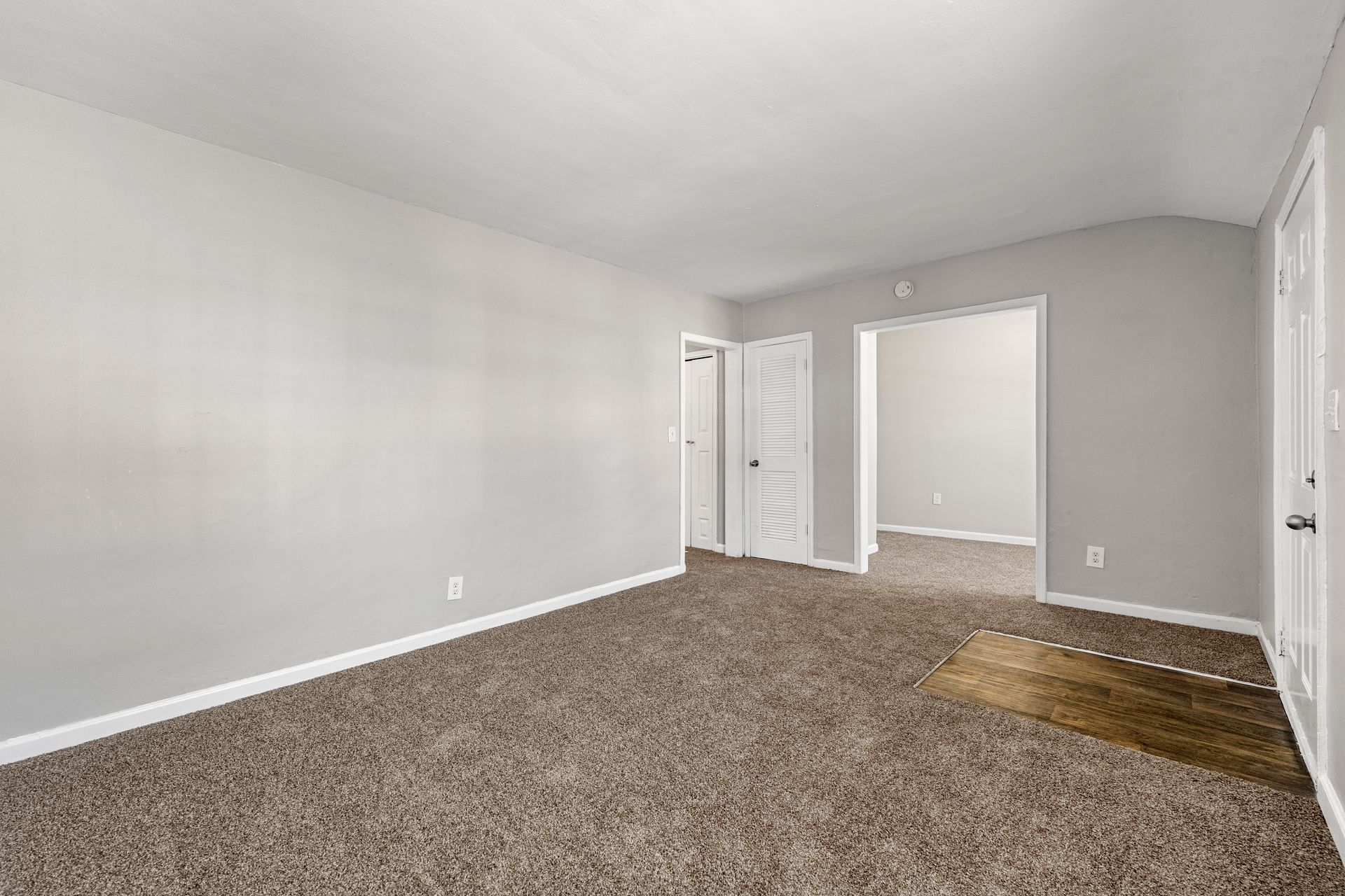 Empty gray bedroom with beige carpet and an open doorway to a hall and adjacent room