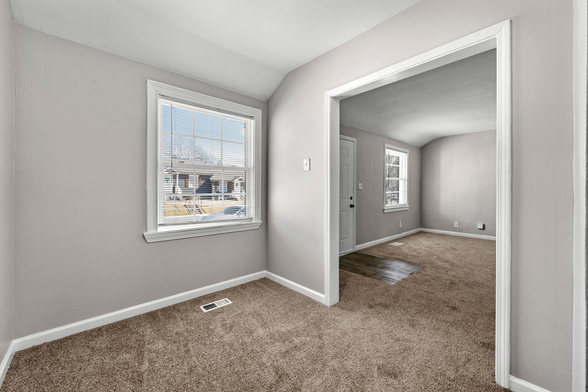 Empty carpeted room with light gray walls, a window, and an open doorway to another room