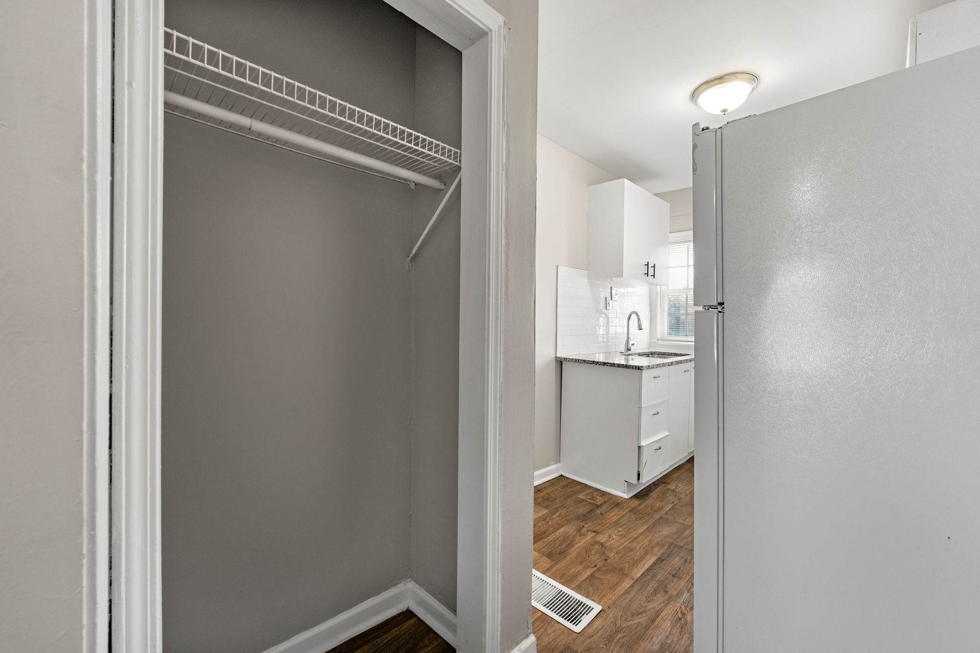 Empty closet next to a bathroom with white cabinets and wood flooring