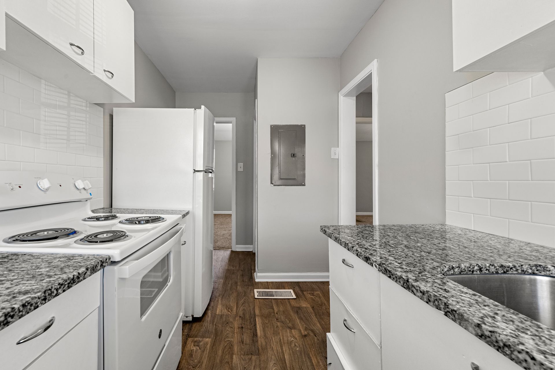 Bright white galley kitchen with granite countertops, white appliances, and wood flooring