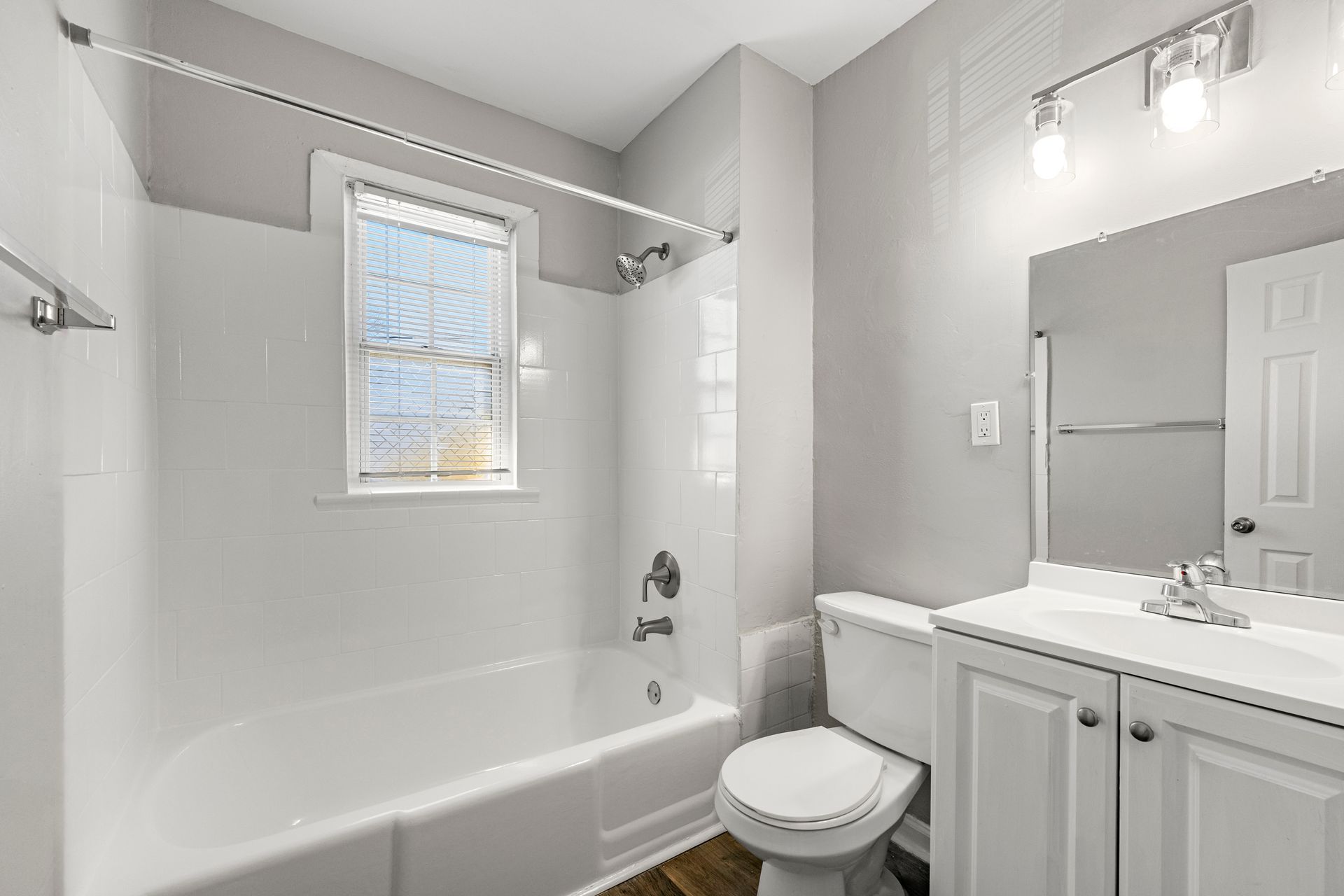 Bright white bathroom with tub-shower, window, toilet, and vanity with mirror lights