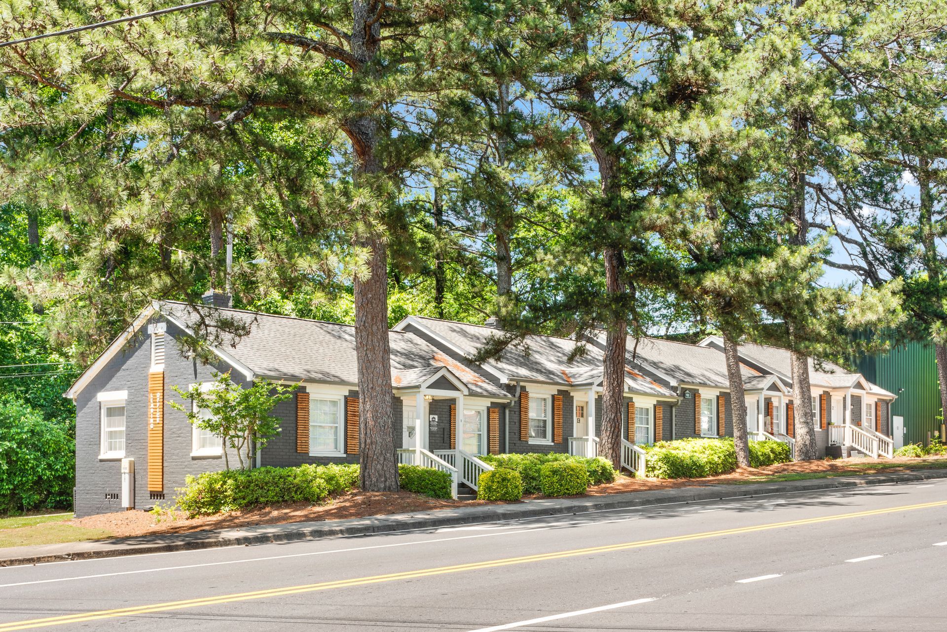 Row of small gray townhouses with white trim along a tree-lined street