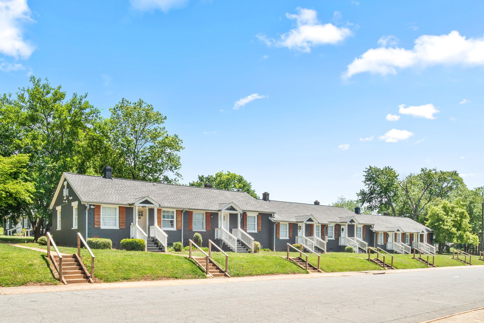 Row of gray cottages with red doors along a tree-lined road under a bright blue sky