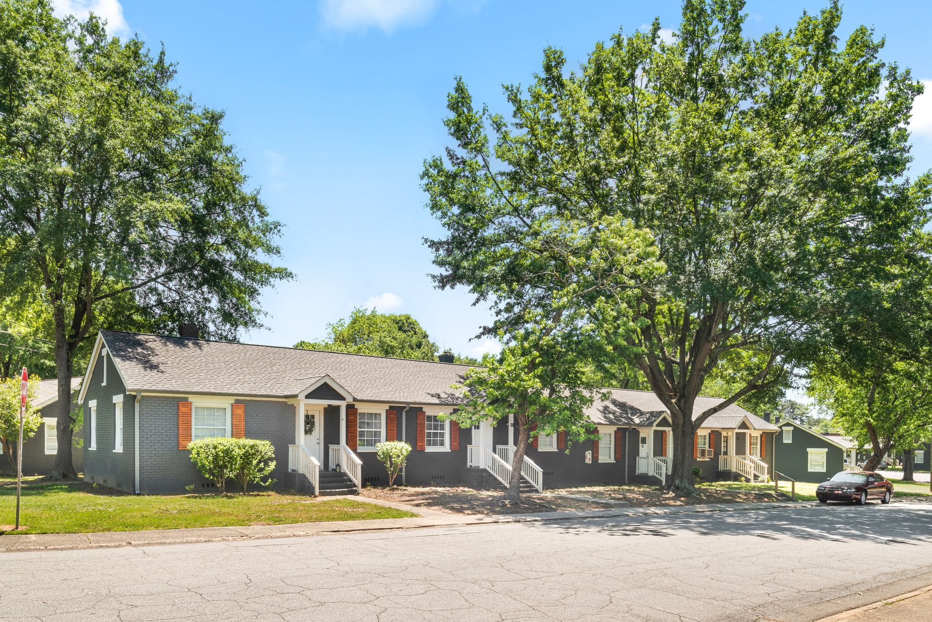 Single-story brick apartment building with trees and parked cars on a sunny street