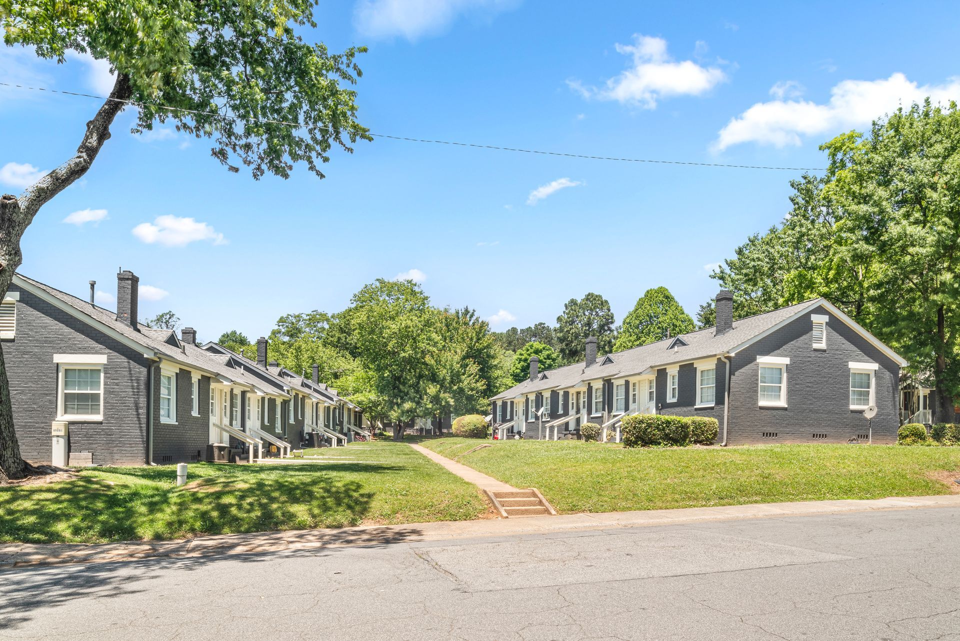 Row of gray cottages with white trim along a grassy lane under a blue sky