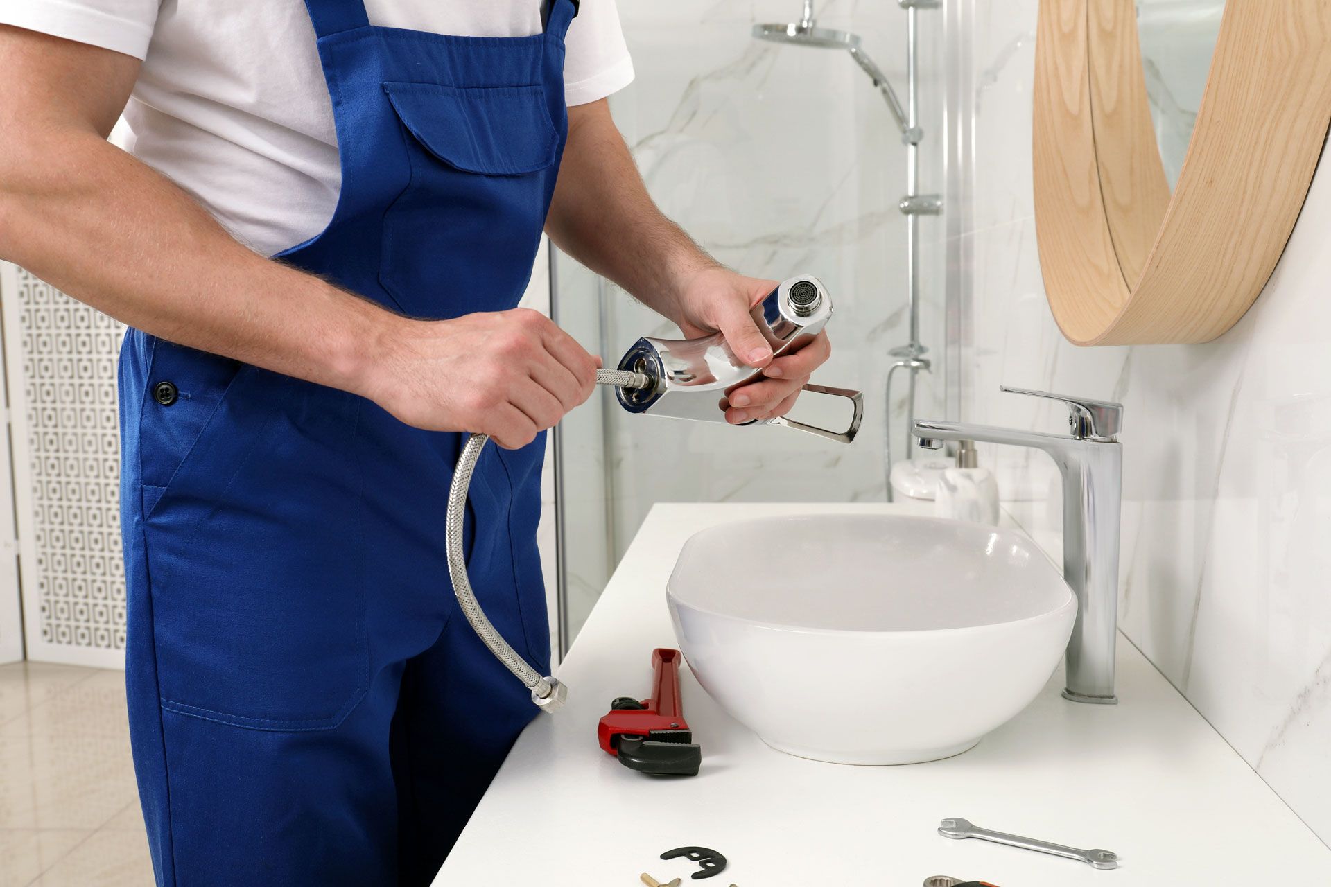 Plumber in blue overalls installing a faucet over a white bathroom sink
