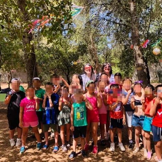 Bambini e due adulti all'aperto, in posa per una foto; alberi sullo sfondo.