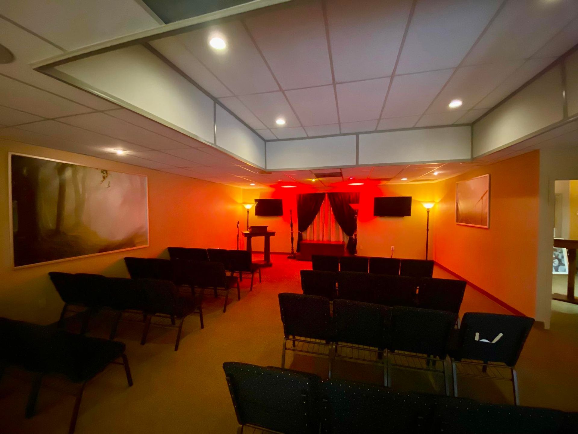 Empty small stage room lit in red with rows of chairs and speakers on both sides