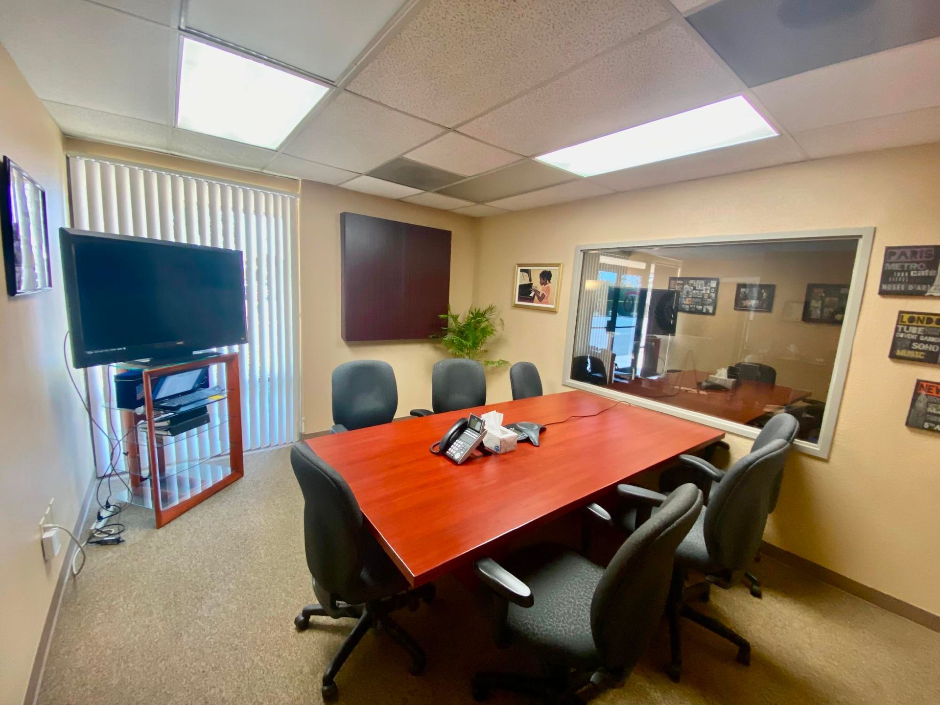 Conference room with red table, black chairs, TV, and glass wall under fluorescent lights