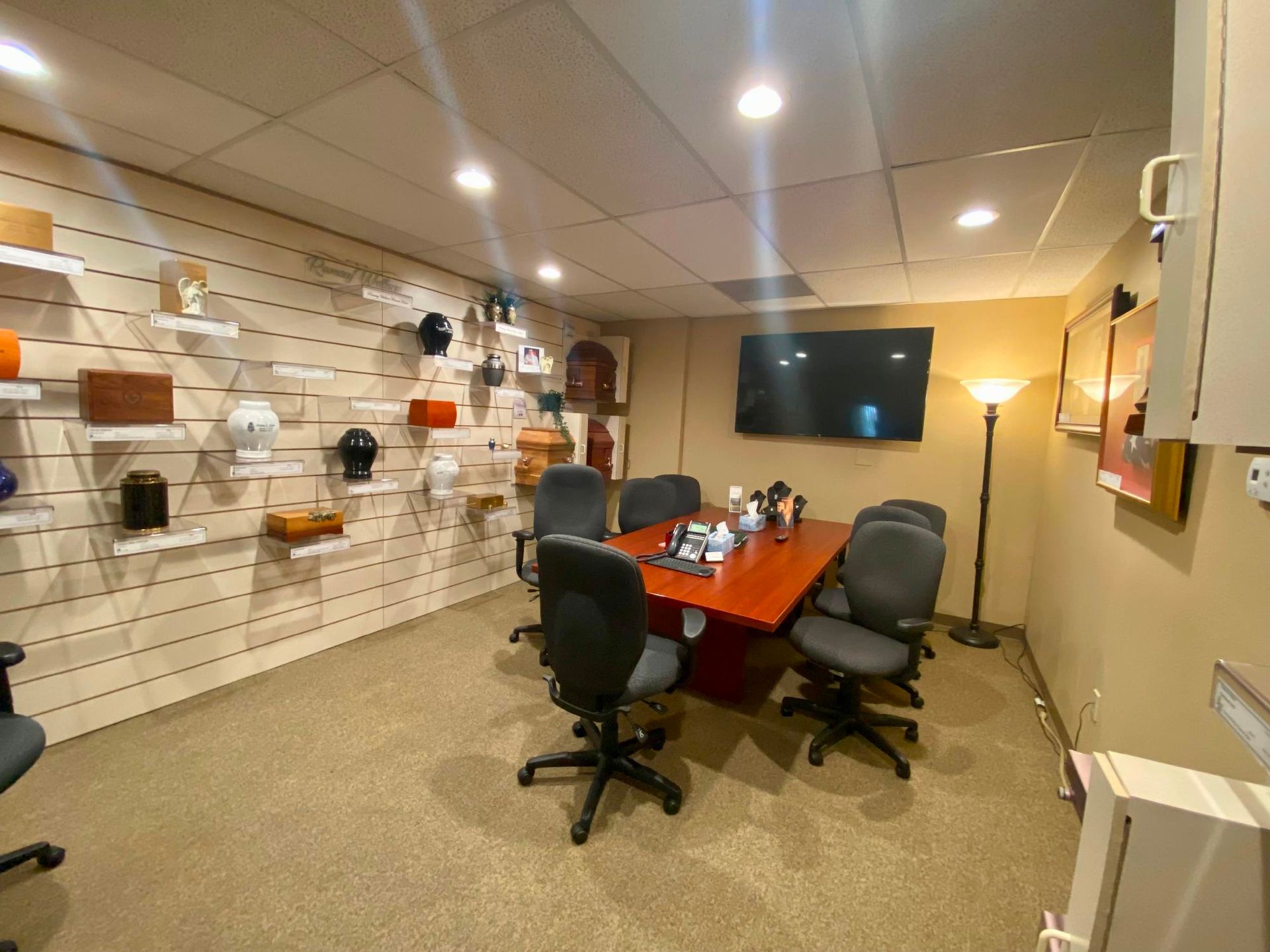 Modern conference room with a red table, black chairs, wall-mounted TV, and decorative wall shelving