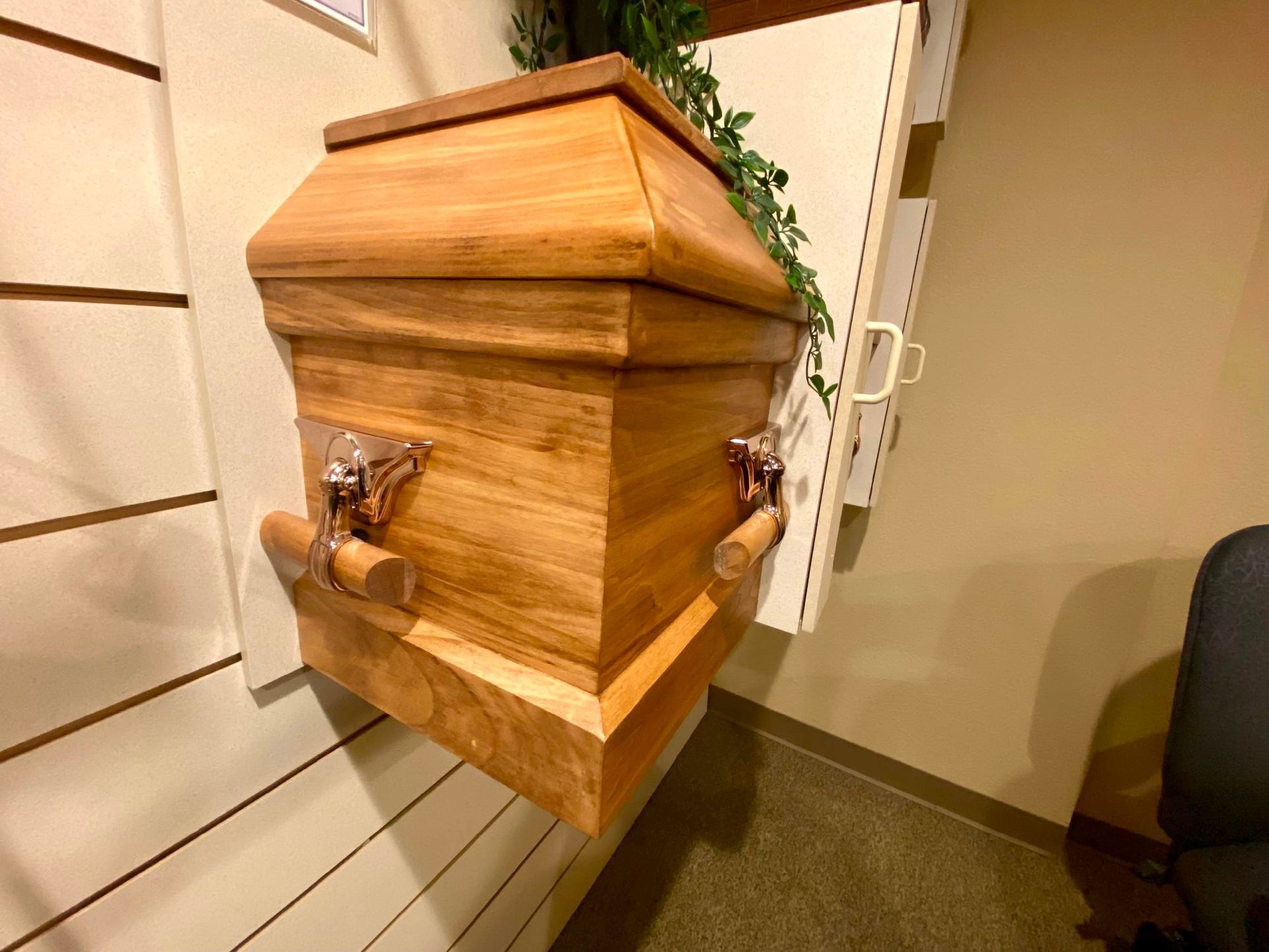Wooden urn-style planter with brass handles, mounted on a wall in a hallway.