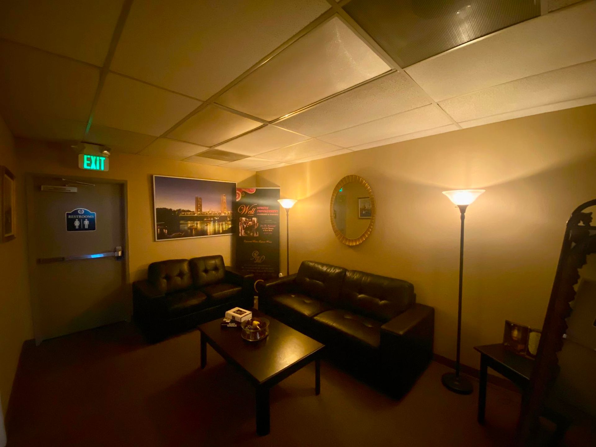 Dim waiting room with leather couches, coffee table, floor lamp, wall art, and warm lighting.