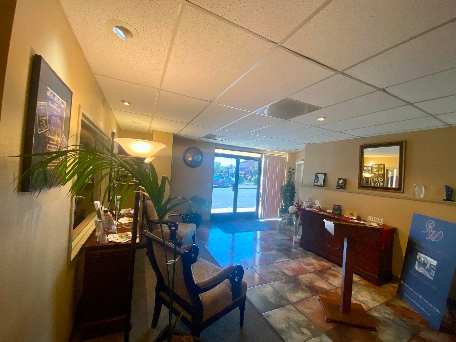 Office lobby with red front desk, chair, wall art, and large windows.