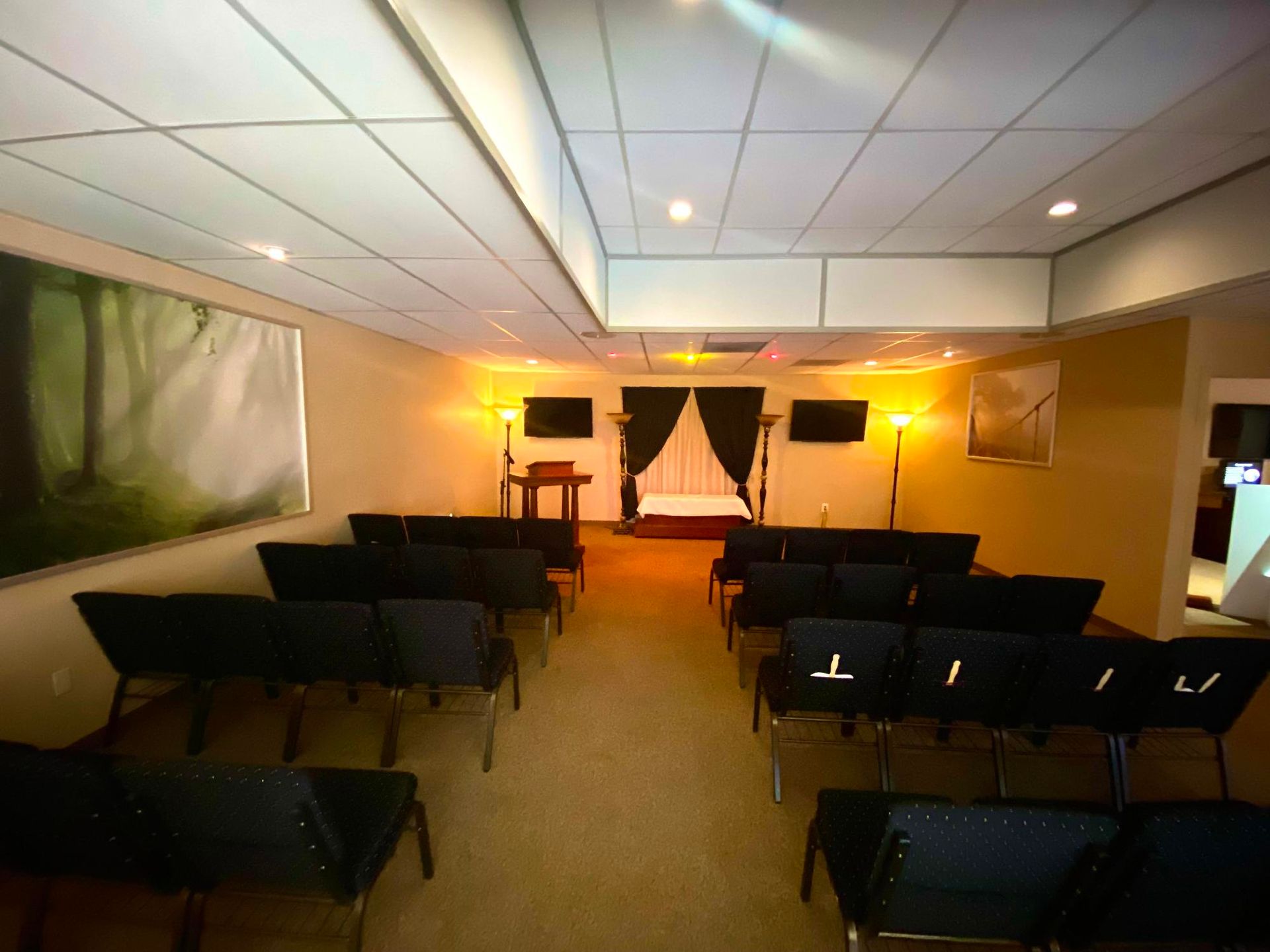 Small empty conference room with rows of black chairs facing a lit stage and white draped backdrop.