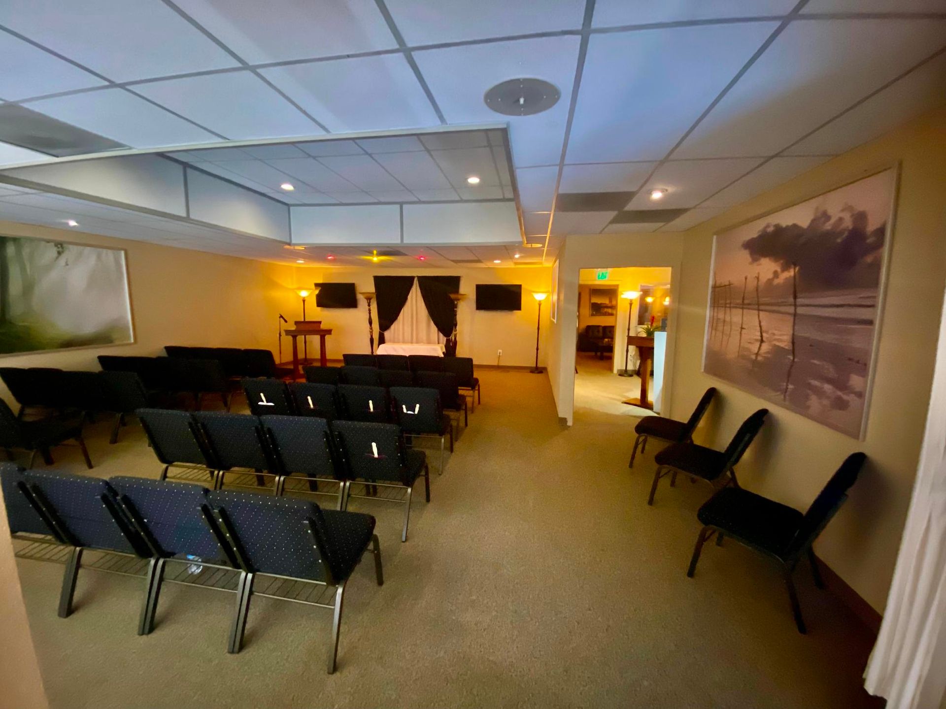 Empty conference room with rows of black chairs, projector screen, and warm wall lighting