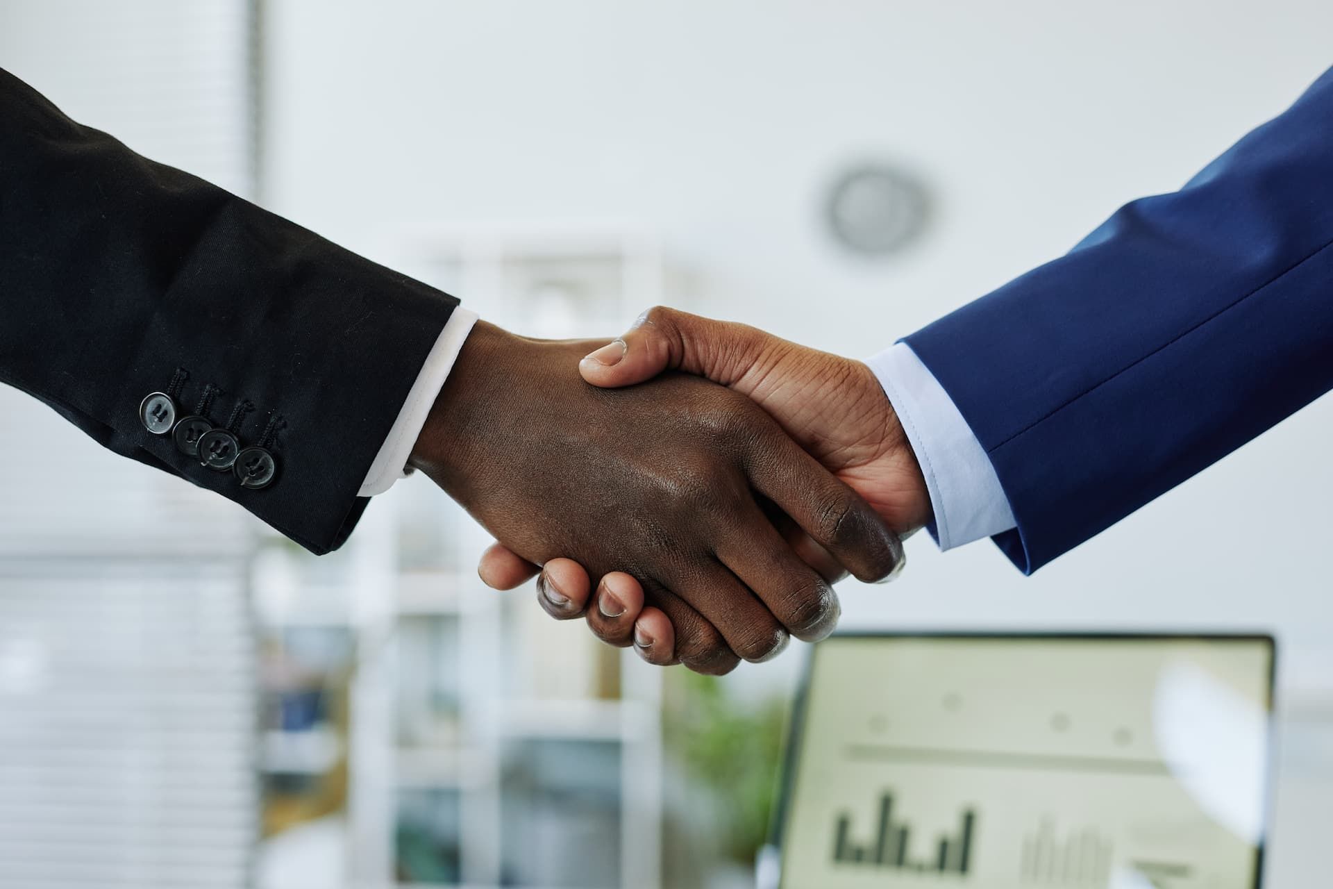 Two people in dark suits shaking hands in an office setting