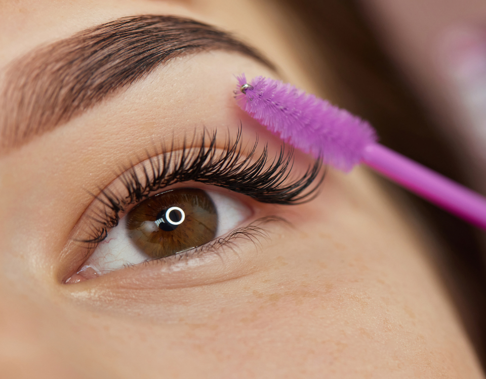 Eine Frau trägt mit einem lila Pinsel Wimperntusche auf ihre Augen auf.