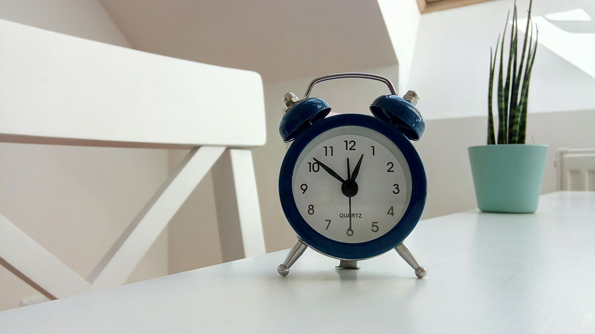 A blue alarm clock shows the time at approximately 10:05, sitting on a white table next to a small potted plant.