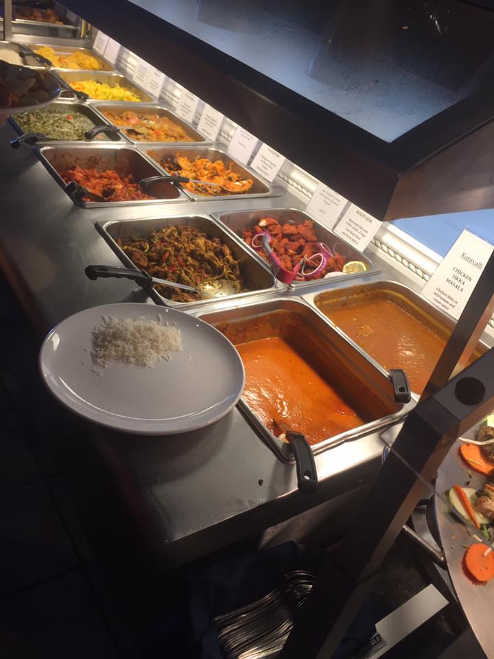 Indian buffet with various dishes; a plate of rice is ready to be filled.