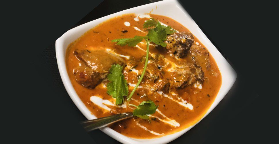 Chicken tikka masala in a white bowl, garnished with cilantro and cream, on a dark surface.