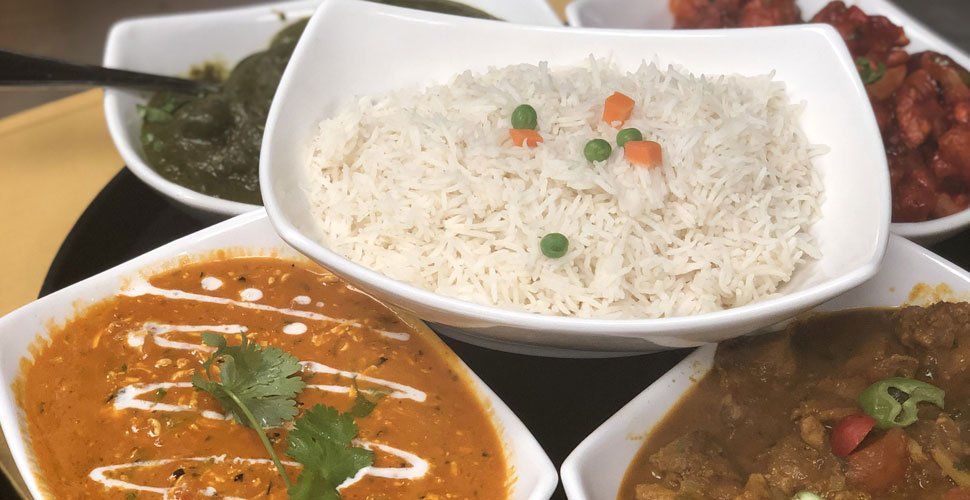 Indian food spread: rice, curries, and spinach in white bowls, on a black plate.