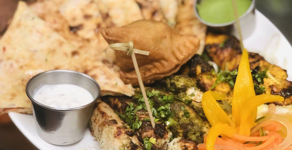 Plate of Indian appetizers, including naan, samosa, grilled meats, and dipping sauces.