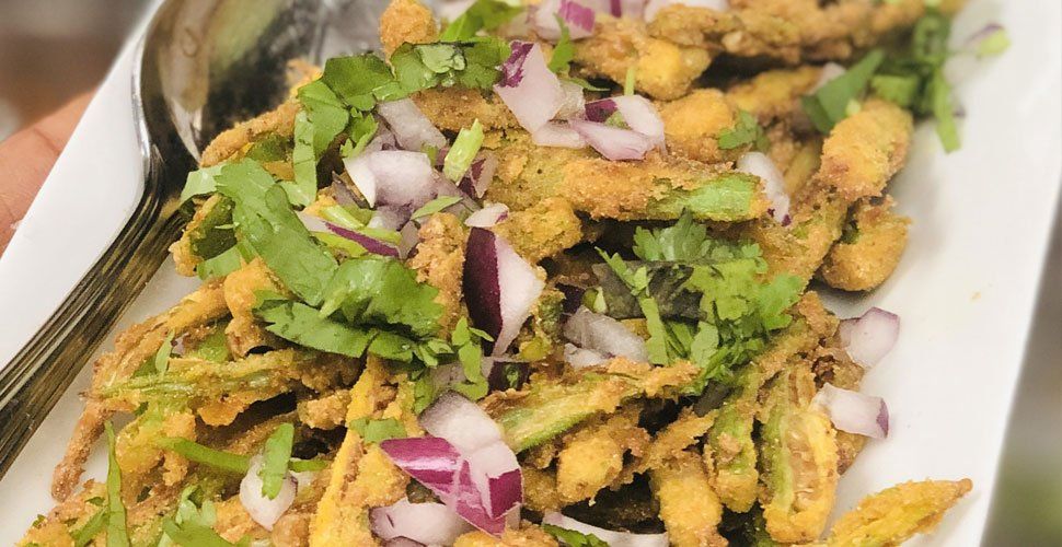 Fried okra garnished with red onion and cilantro on a white plate.
