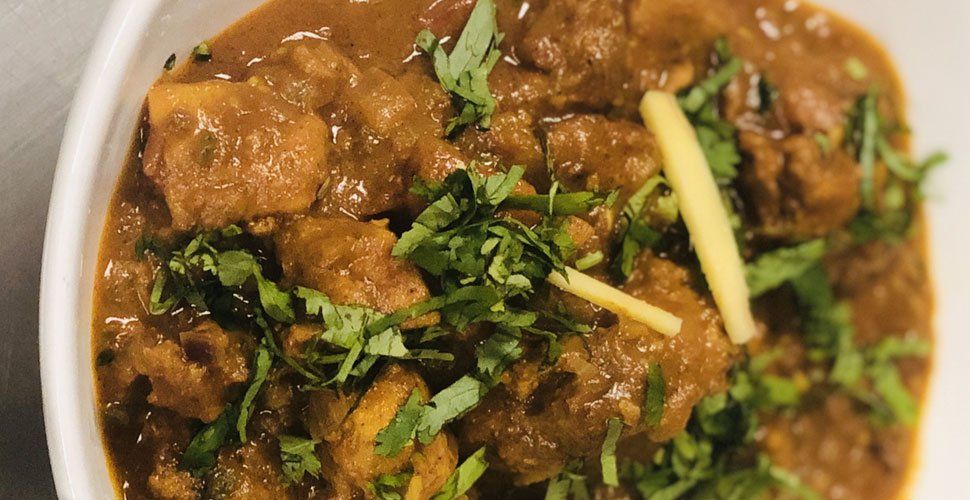 Chicken curry in a white bowl, garnished with cilantro and ginger.
