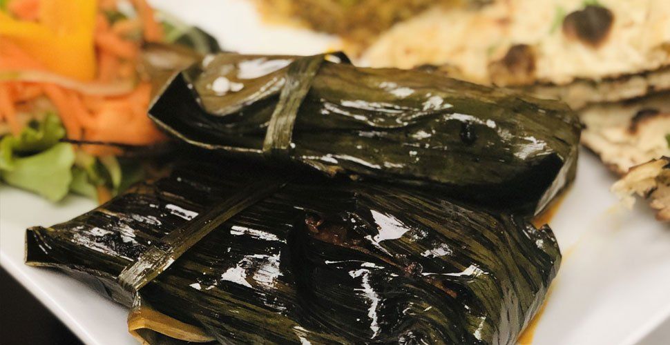Dark, glossy wrapped food on a white plate with side dishes, naan, and vegetables.