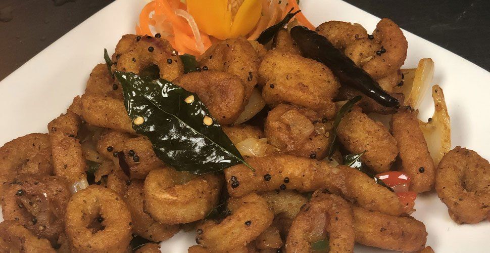 Golden fried calamari with curry leaves and spices on a white plate.