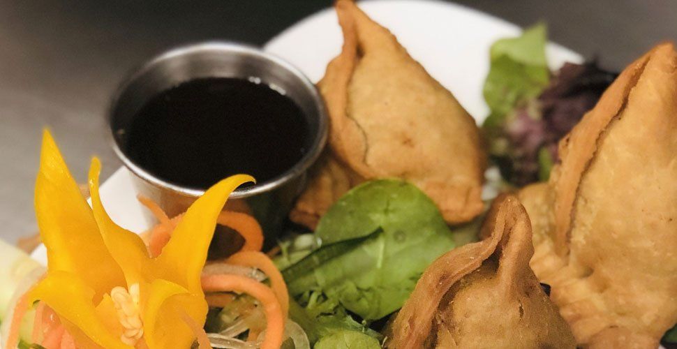 Samosas with dipping sauce and salad, arranged on a plate.