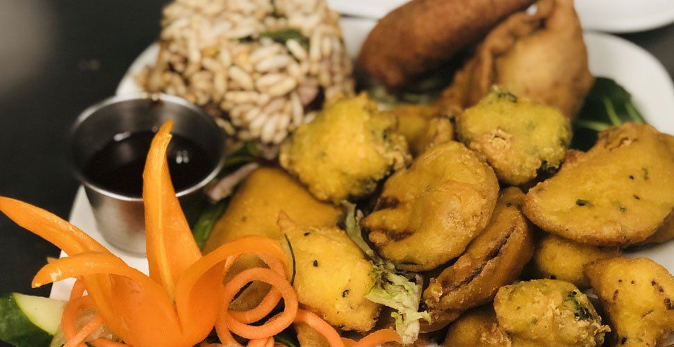 Plate of assorted Indian fried snacks with dipping sauce and carved carrot garnish.