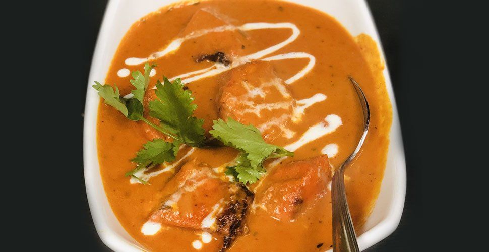 Bowl of creamy orange-red food, likely curry, with white swirls of cream and cilantro garnish.