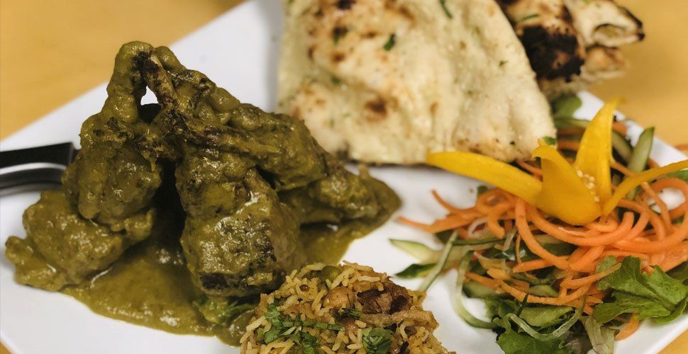 Chicken in green sauce with naan bread, rice, and a small salad on a white plate.