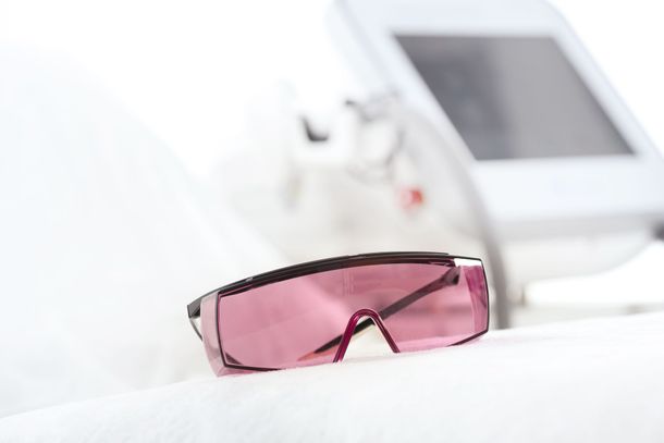 Pink-tinted eyeglasses on a white surface with a blurred medical device in the background