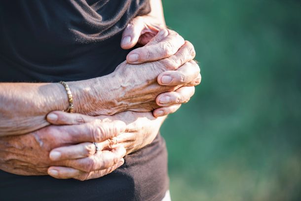 Older hands clasping a forearm against a blurred green background
