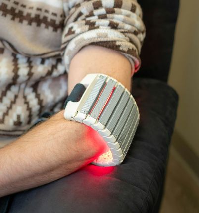 Arm with a gray wrist brace emitting a red light, resting on a dark cushion.