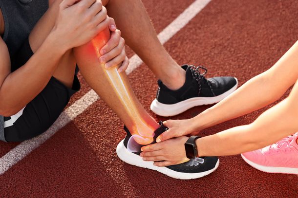 Athletes passing a baton in a relay race on a red track, with hands and black running shoes visible