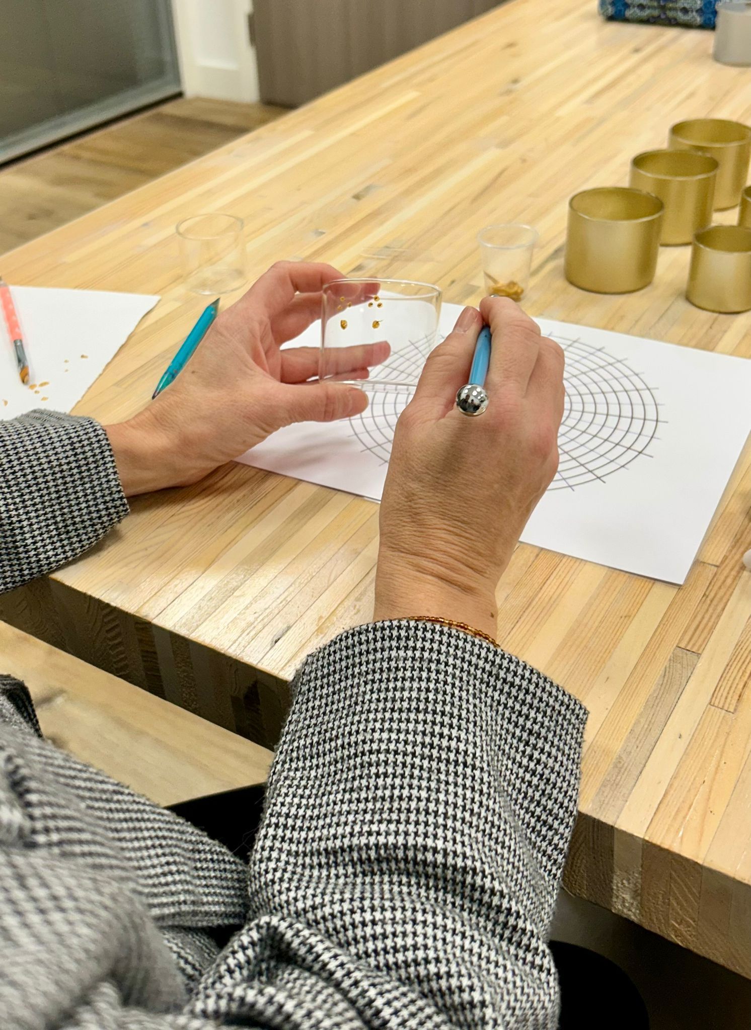 Een persoon gebruikt een potlood om een ​​cirkelvormig ontwerp in te kleuren; gouden bakjes staan ​​op tafel.