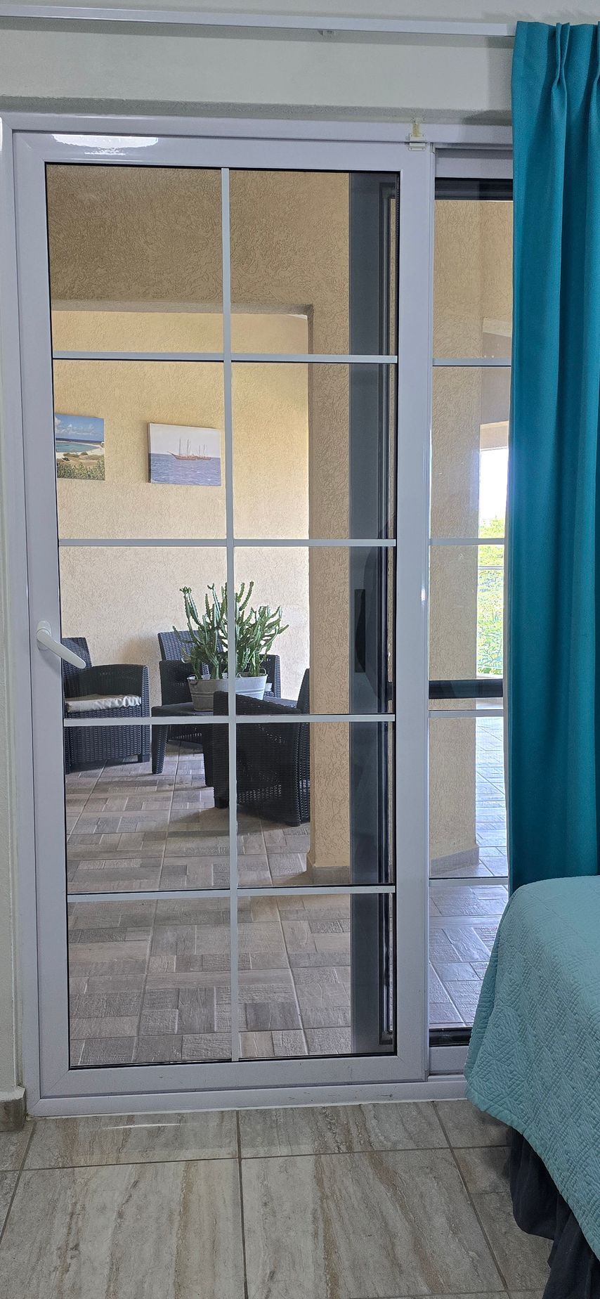Sliding glass door with white frame, blue curtains, and a view into a room with stairs and a plant outside