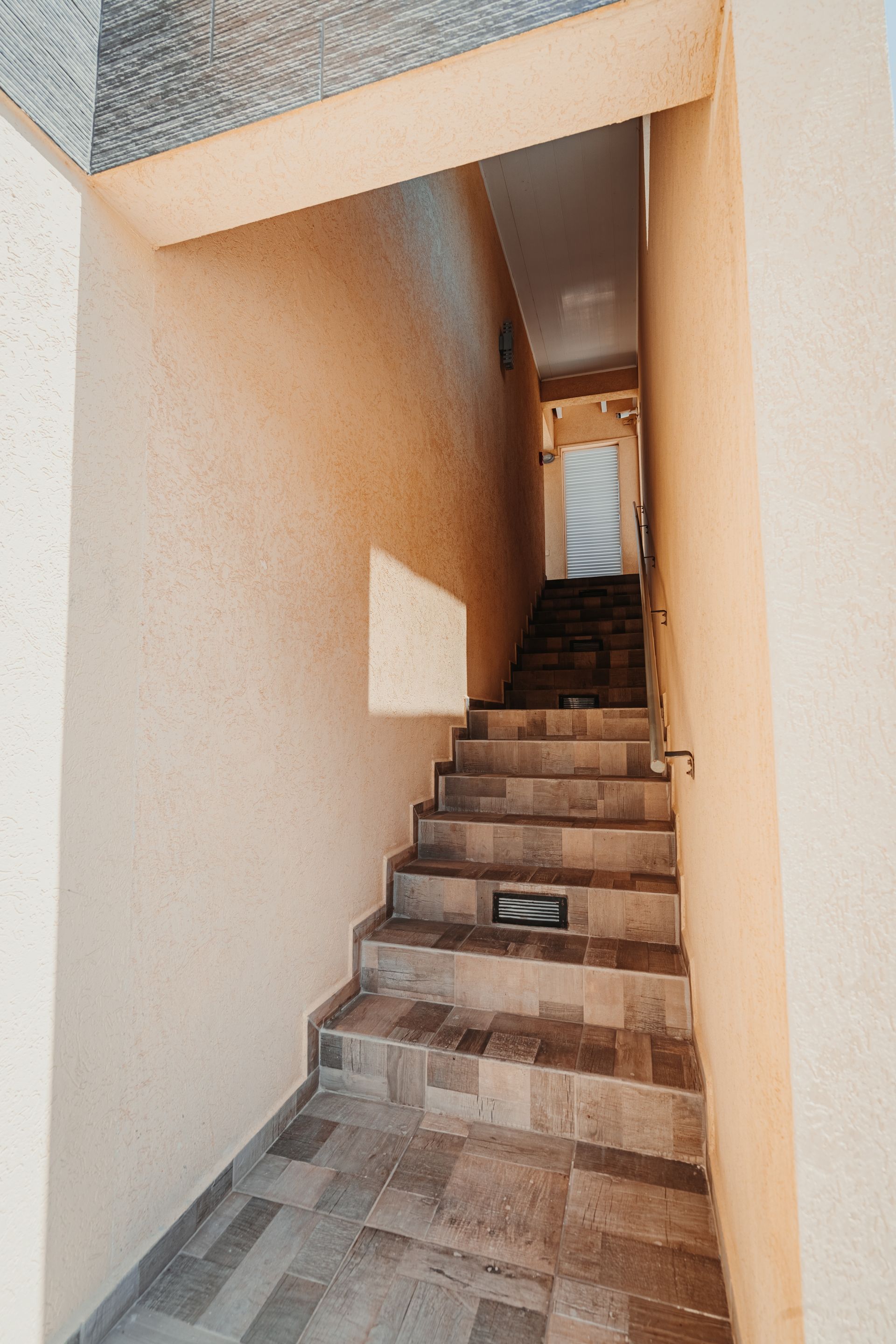 Narrow outdoor stairway between beige walls leading upward to a bright opening