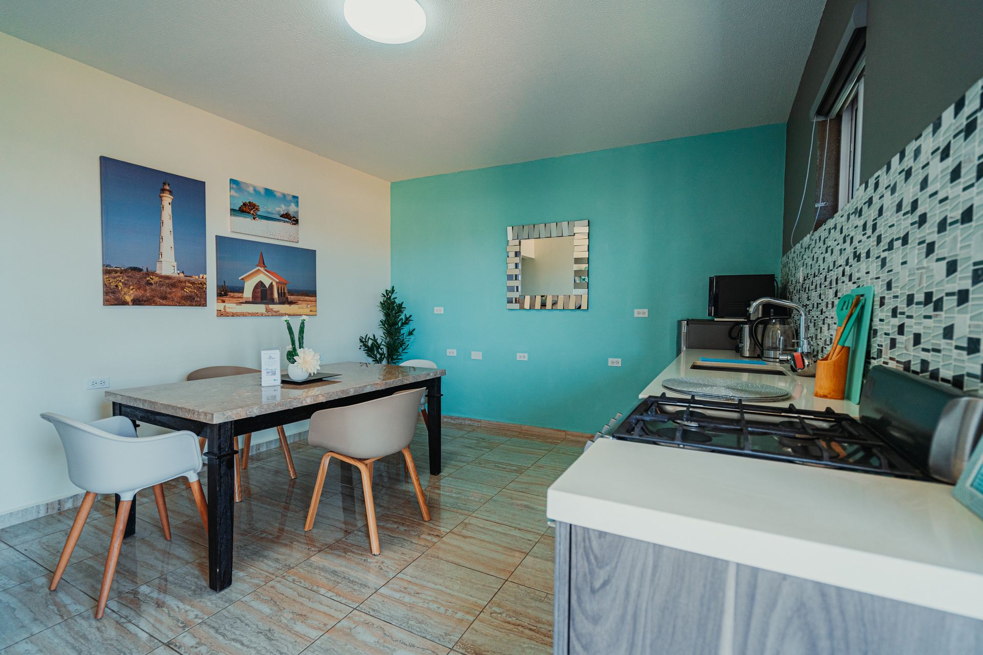 Bright modern kitchen-dining area with teal walls, table, stools, patterned tile floor, and countertop appliances