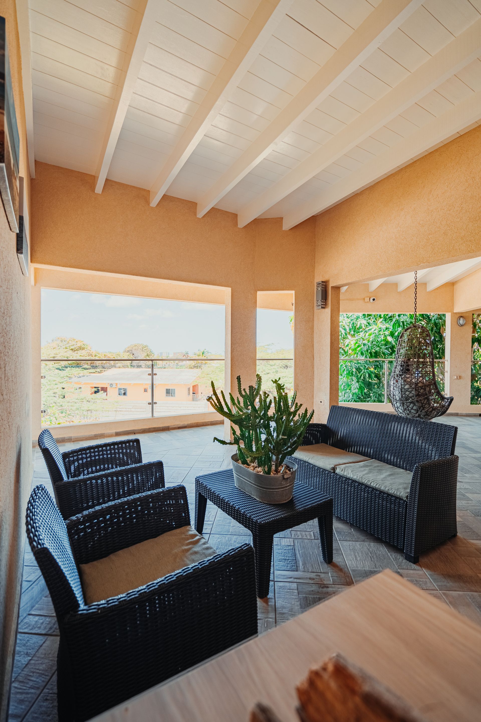 Outdoor patio seating area with wicker chairs, tables, and white beamed ceiling