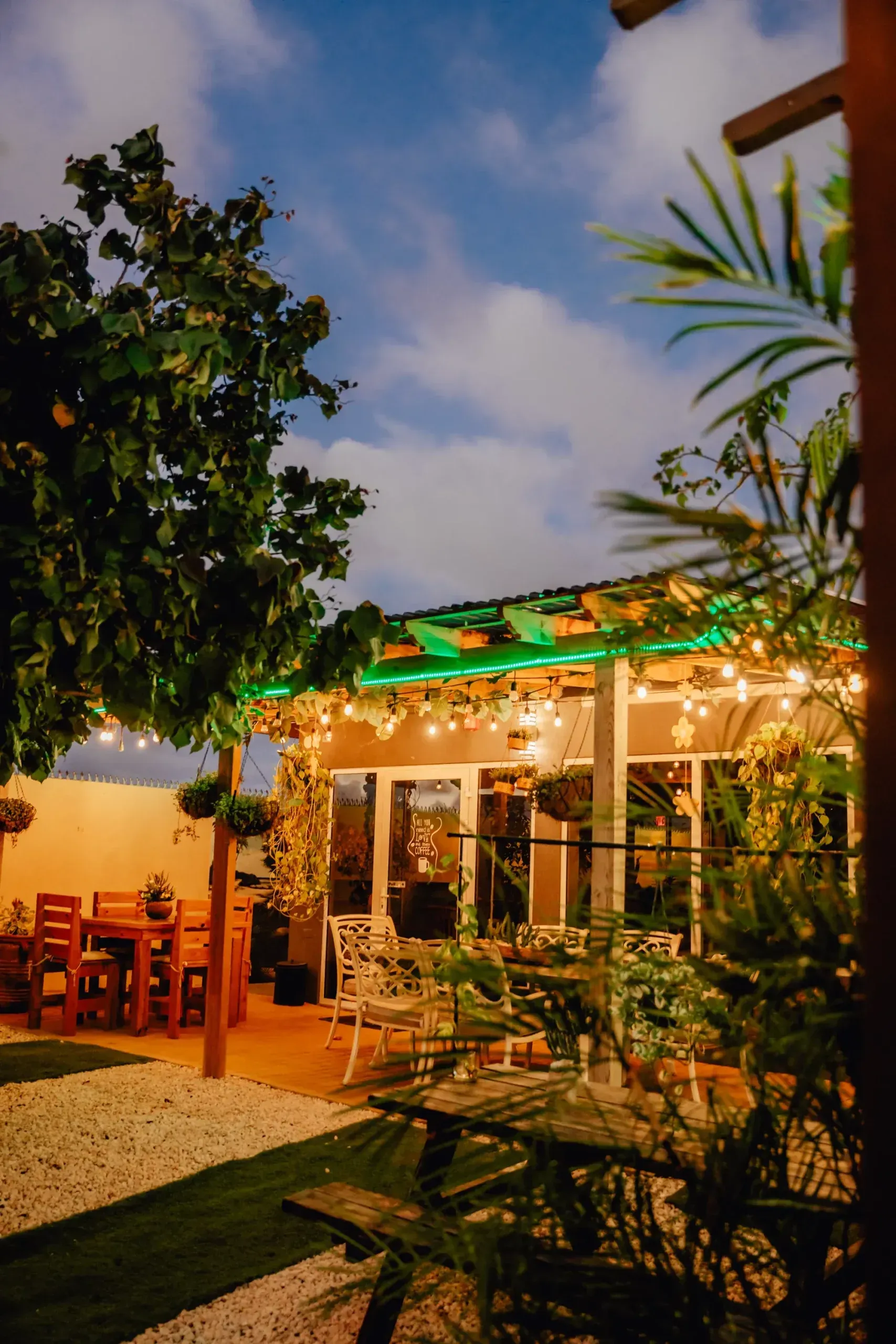 A patio with tables and chairs and a green roof at night.